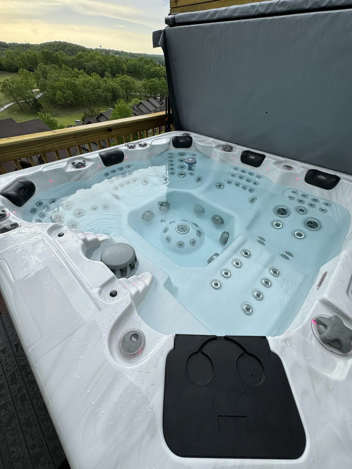 The hero image shows the condo's private wooden deck surrounded by the lush Ozark landscape, featuring a bubbling hot tub that invites guests to relax and soak in the tranquil ambiance. The deck overlooks rolling hills and captures the soft colors of sunset, creating an inviting outdoor space for unwinding or socializing.