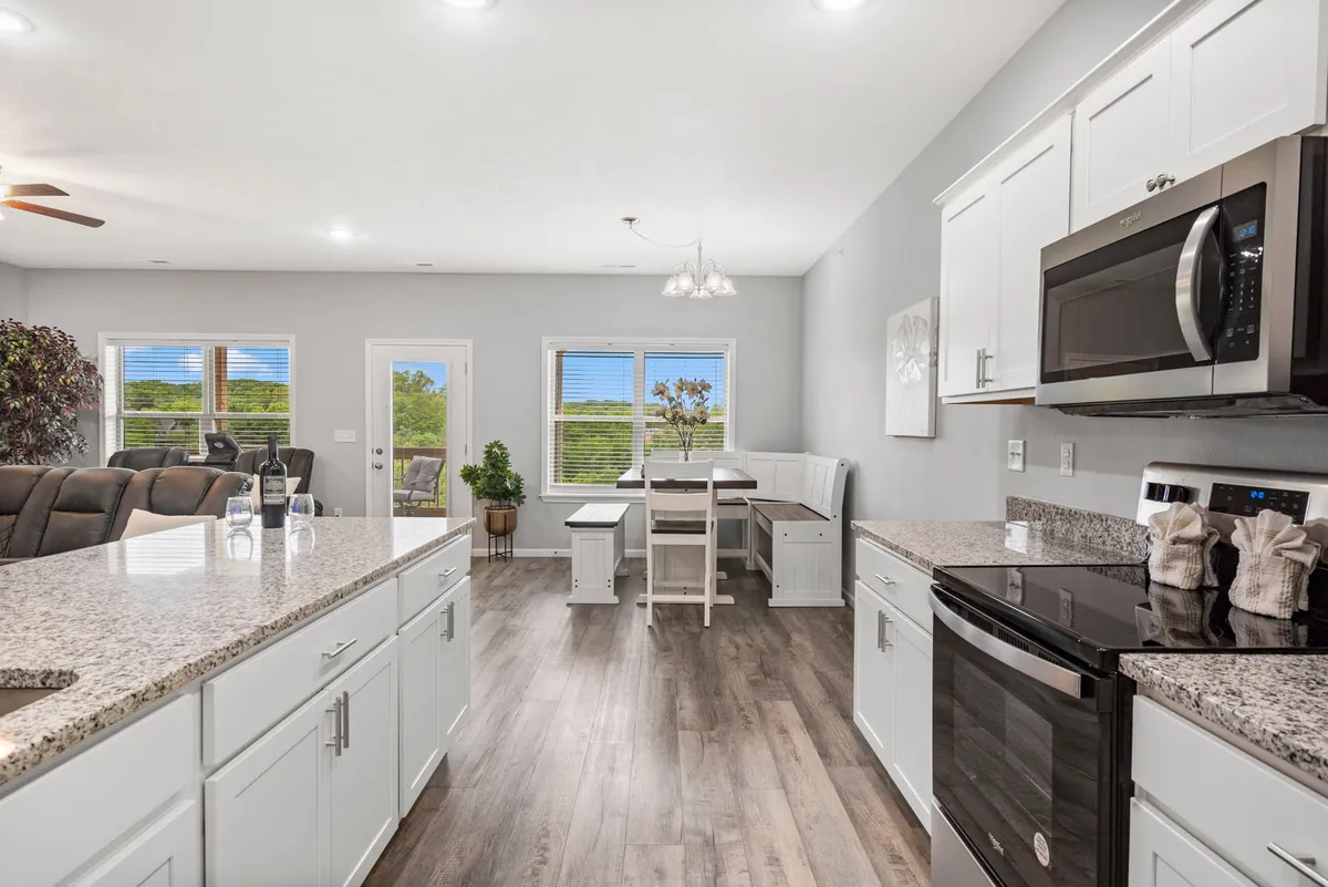 A bright and cheerful interior shot with a granite kitchen countertop in the foreground, adjacent to a stylish dining area and windows framing lush greenery. Modern appliances are visible, and the overall atmosphere is warm and inviting, ideal for group meals and gatherings.
