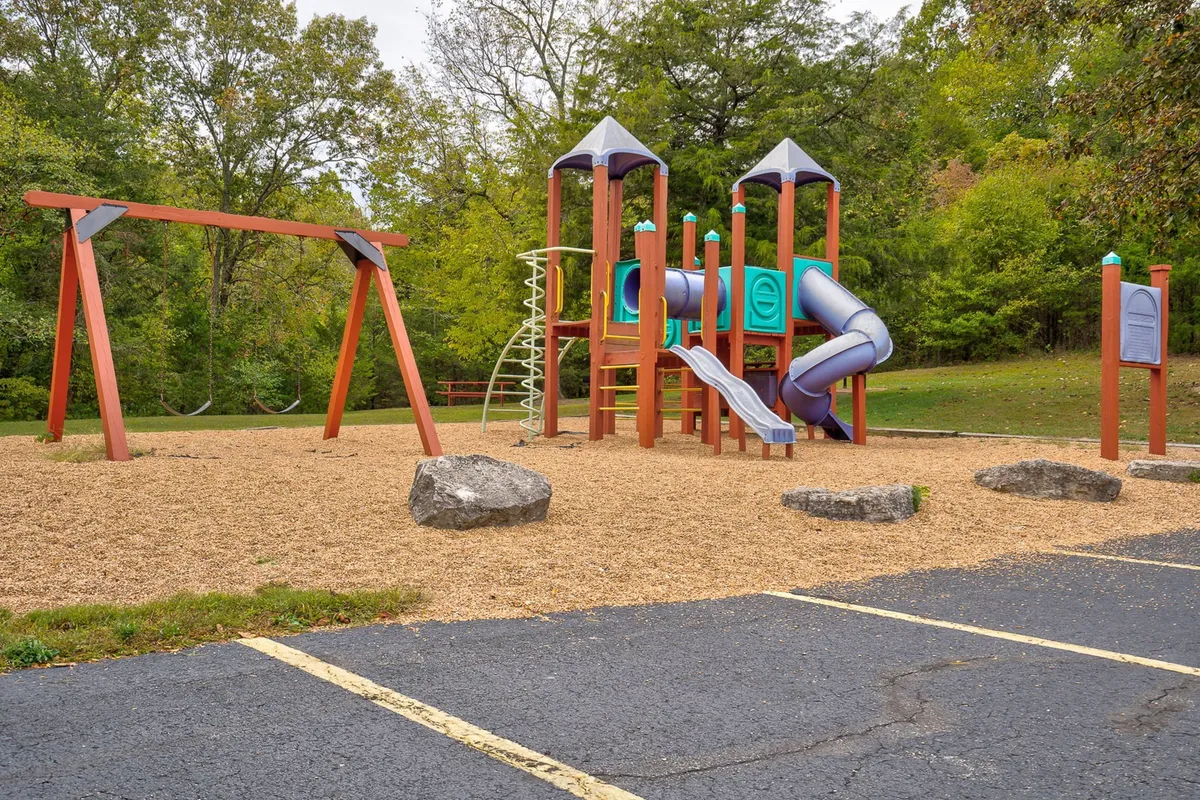 A colorful playground featuring a sturdy structure, swings, and playful rock formations, surrounded by natural landscaping. The area is designed for children and family fun, with ample space for kids to roam and play.