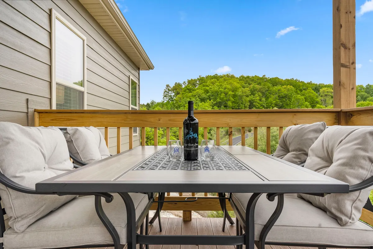 This image presents an exterior deck with a dining table, wine bottle, comfortable seating, and lush green landscape in the background. It radiates a peaceful, sociable vibe, showcasing the deck as a versatile space for both relaxation and connection with nature.