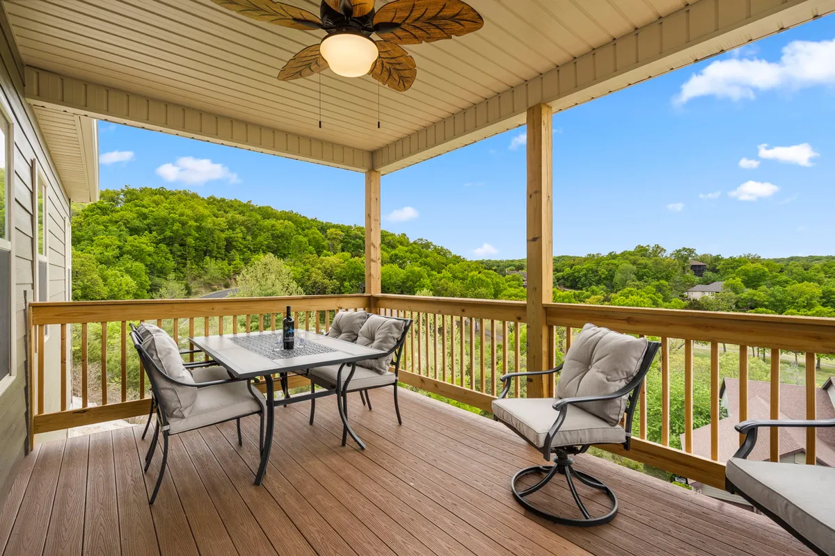 An inviting exterior patio is featured, complete with a comfortable outdoor dining table and chairs, ceiling fan, and a peaceful natural landscape in the background. The setting is designed for al fresco dining, leisurely drinks, or simply relaxing in the shade while immersed in the surroundings.