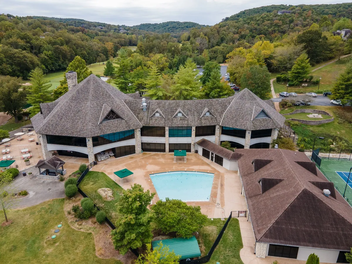 This exterior view showcases a sparkling swimming pool, landscaped gardens, a tennis court, and the main building in the background. The inviting pool area, surrounded by greenery, is ideal for group relaxation and outdoor gatherings, suggesting a blend of leisure and community.