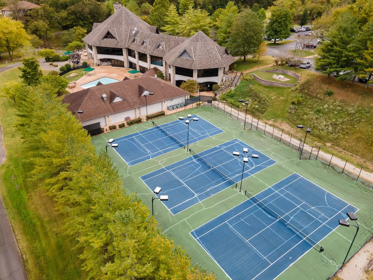 This exterior image features tennis courts and a clubhouse nestled among lush greenery. The scene is lively and welcoming, evoking the spirit of community events and friendly competition. The well-maintained courts and surrounding area suggest an active and social environment, perfect for group gatherings.