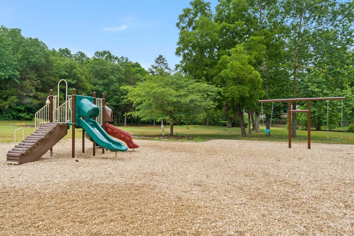 A colorful playground structure featuring slides and a swing set, set in a lush green outdoor space. Children are seen playing and families are nearby, creating an atmosphere of energetic joy and community.