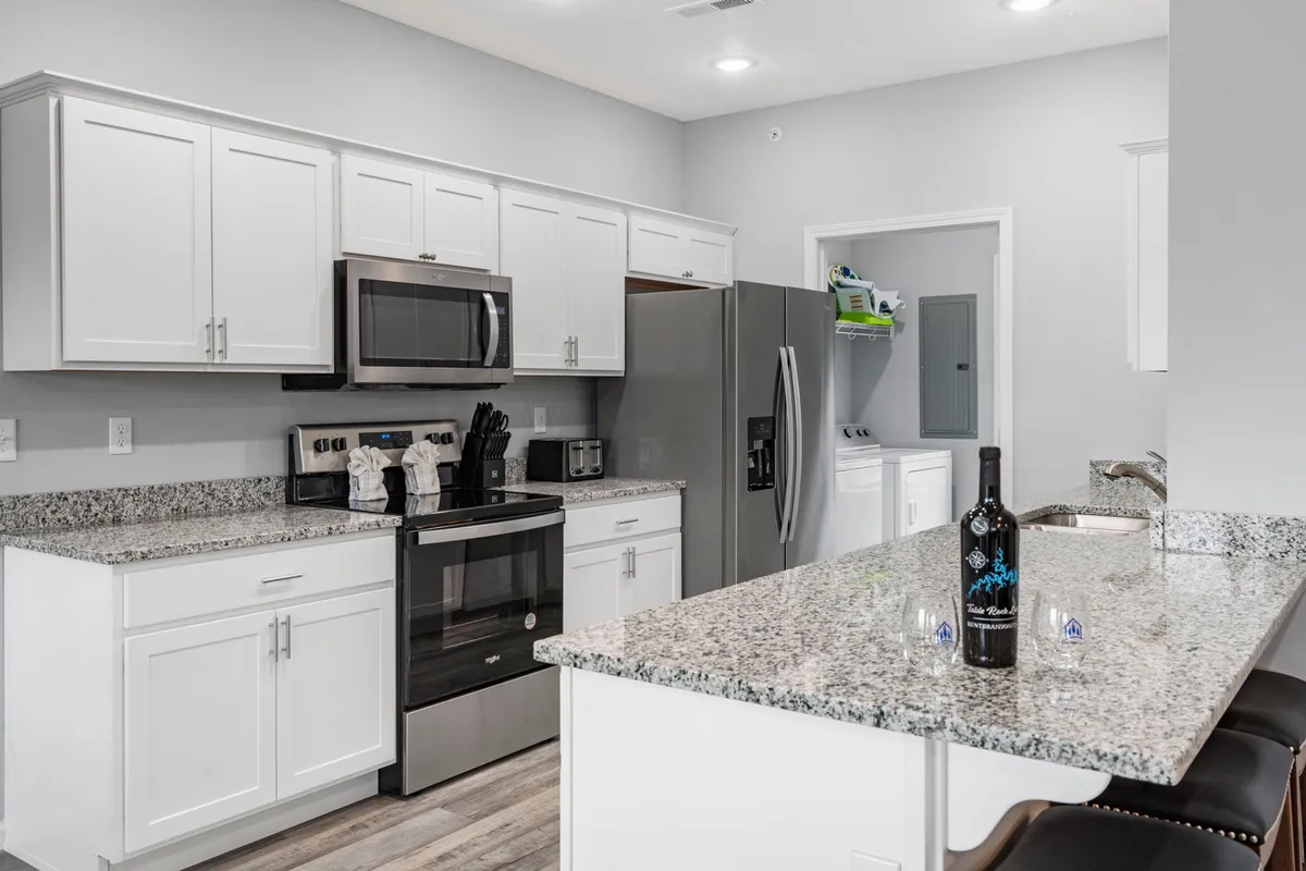 A close-up view of the kitchen area showcases sparkling granite countertops and sleek stainless steel appliances. A wine bottle sits on the counter, suggesting both casual and celebratory gatherings around food and drink.